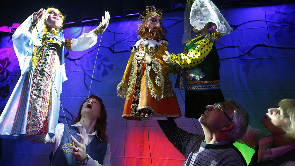 Large puppets are held by puppeteers; puppets are dressed in medieval costumes. 