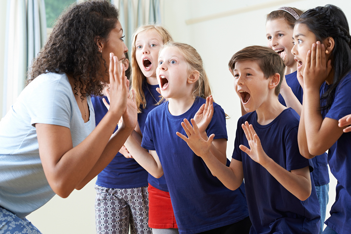 Shocked expressions Six students wearing similar t-shirts have surprised expressions on their faces, their hands raised in front of them, facing their teacher.