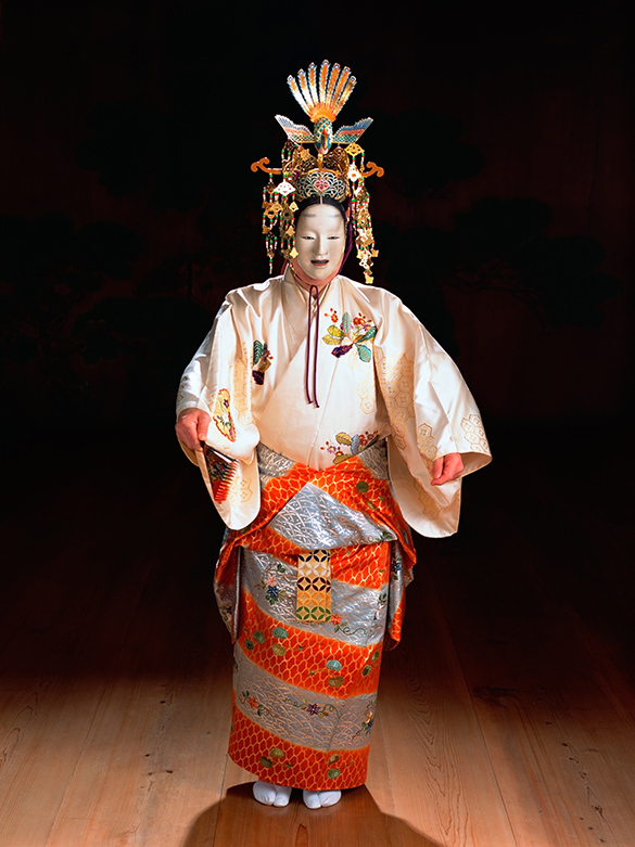 Japanese Noh A performer in an elaborate and colourful Japanese Noh costume stands on a stage under a spotlight, arms out, ready for a performance.