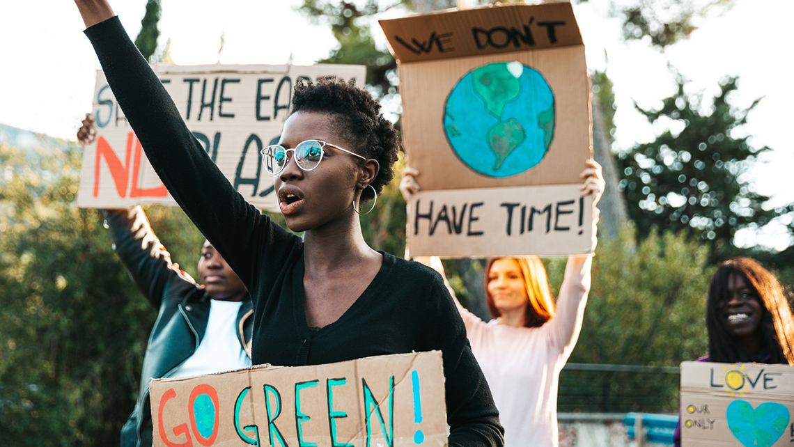 People holding different signs. One of the signs say, “go green”, and another says, “we don’t have time”.