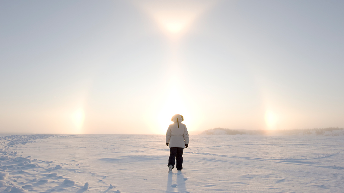 A person wearing a full snowsuit and boots. They are standing on a flat area covered in snow.