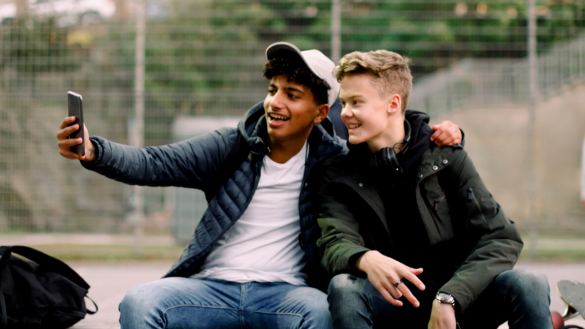 Two male teens at a basketball court taking a selfie.