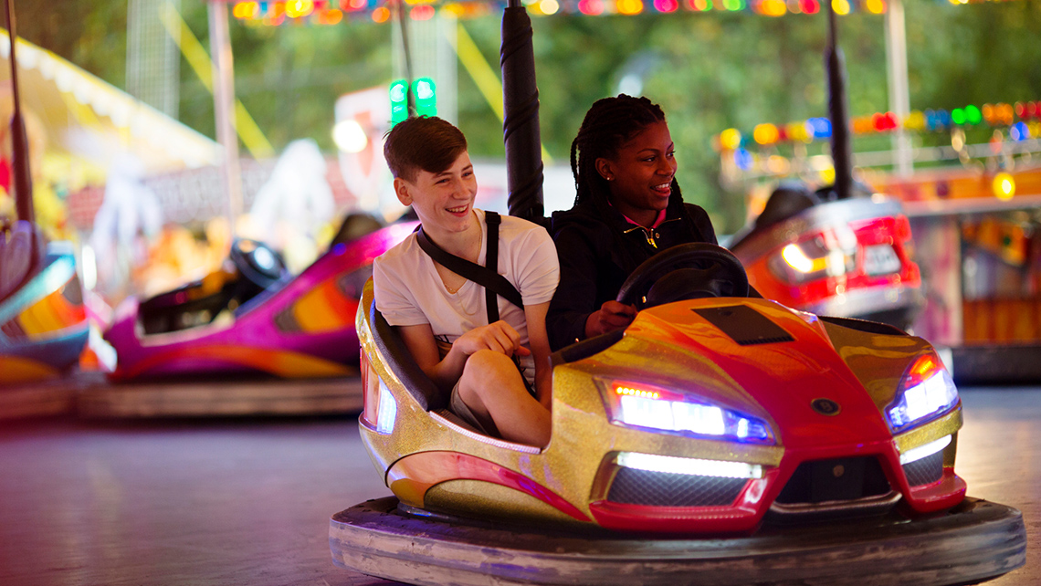 A female teen and male teen riding in a bumper car together.