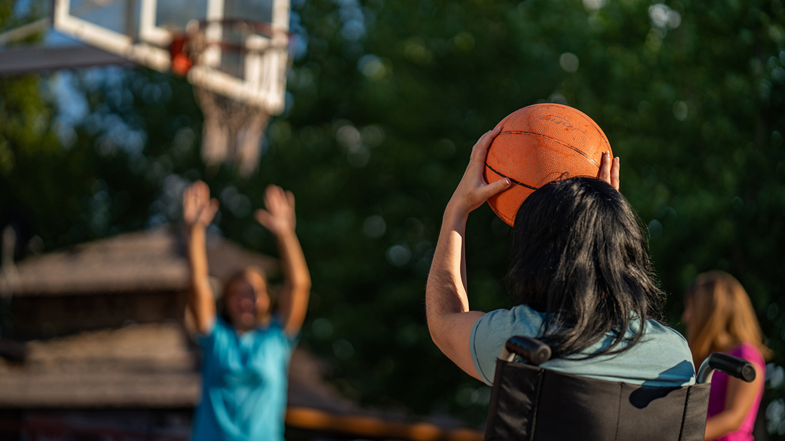 A teen in a wheelchair taking a shot in a basketball game.