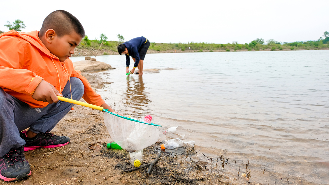 A youth and an adult are collecting empty plastic water bottles that are on a beach.