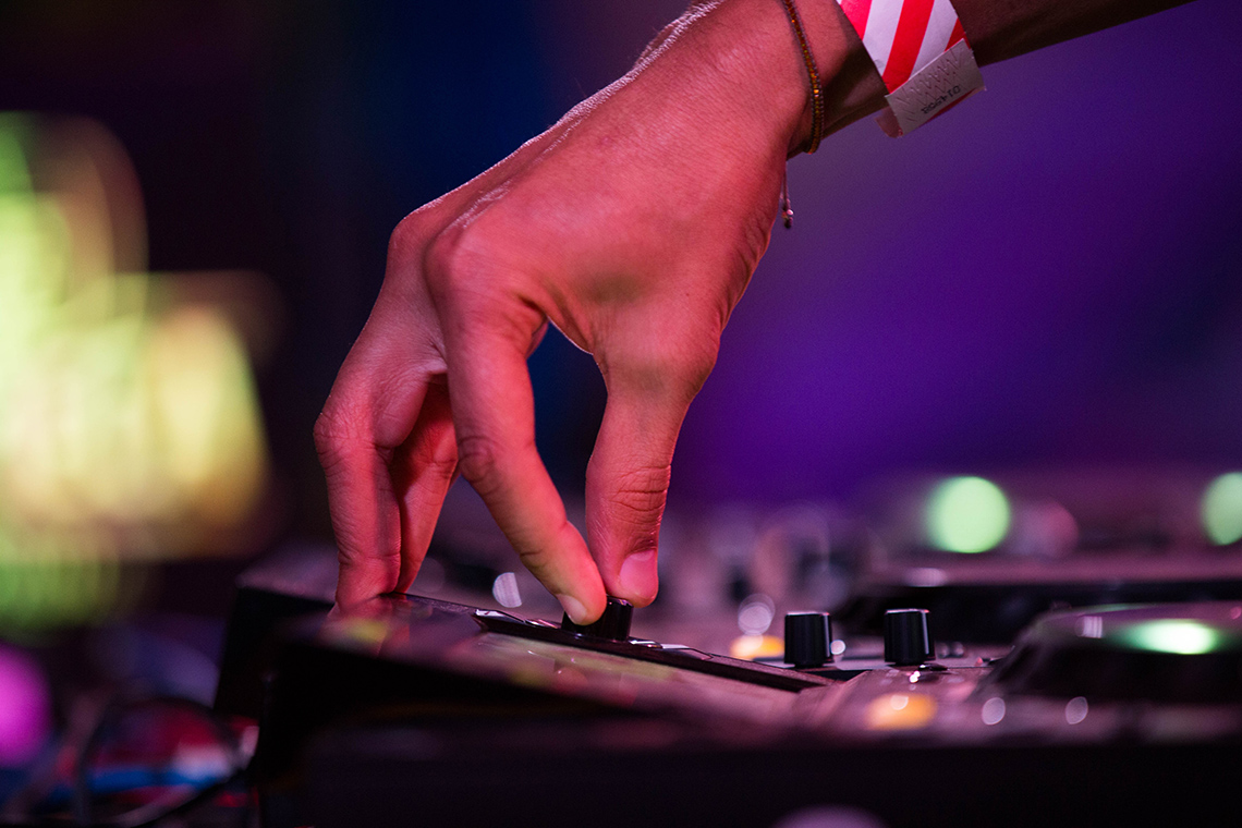 A close-up view of a person’s hand as they use their thumb and index finger to adjust a volume knob on a sound control panel indoors.