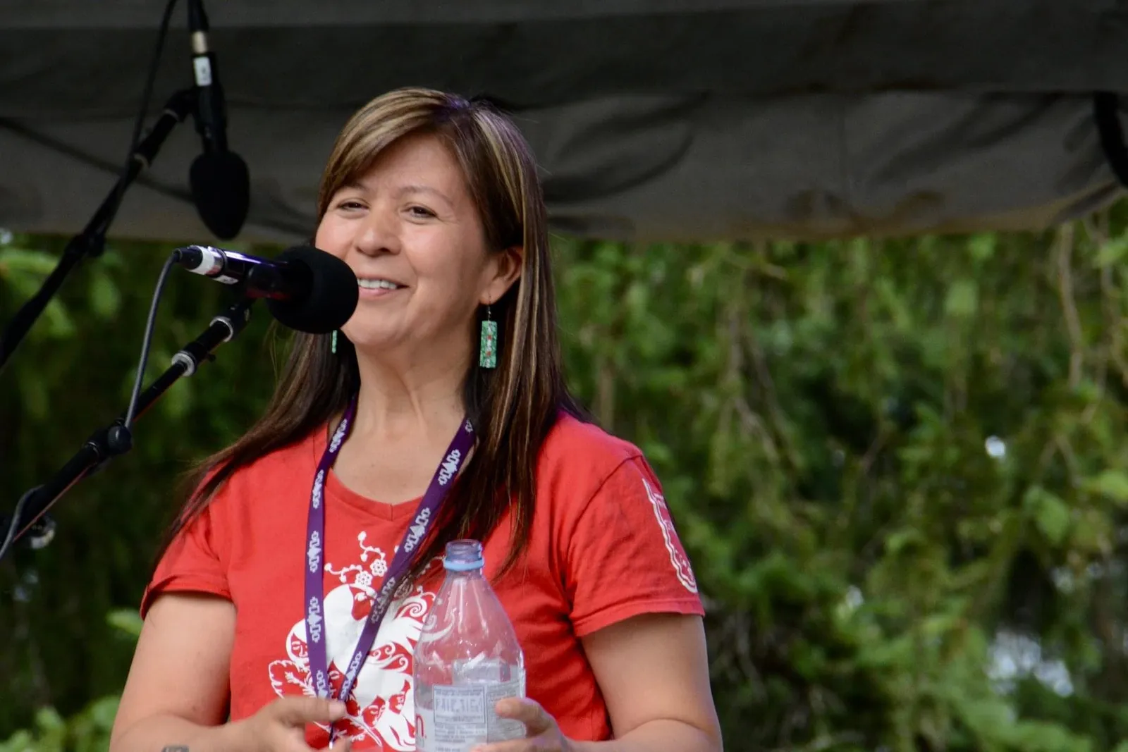 A portrait of singer songwriter Bear Fox, who is standing in front of a microphone and wearing an orange shirt.