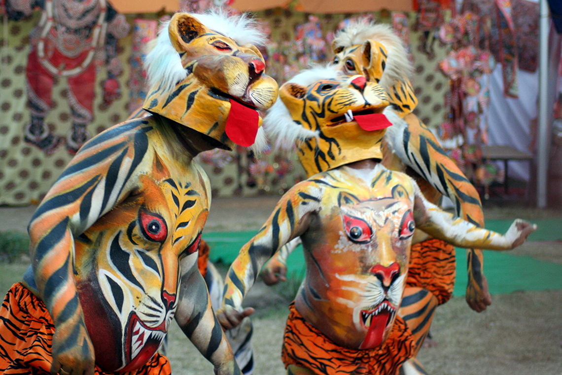 Two people with body paint and paper mache heads resembling tigers are dancing