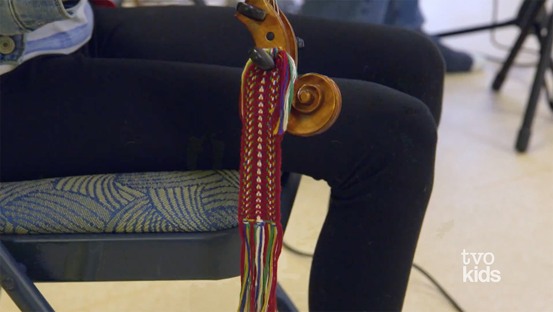 Close up of Morgan’s legs and a piece of her instrument. Looped around the instrument is a red sash.