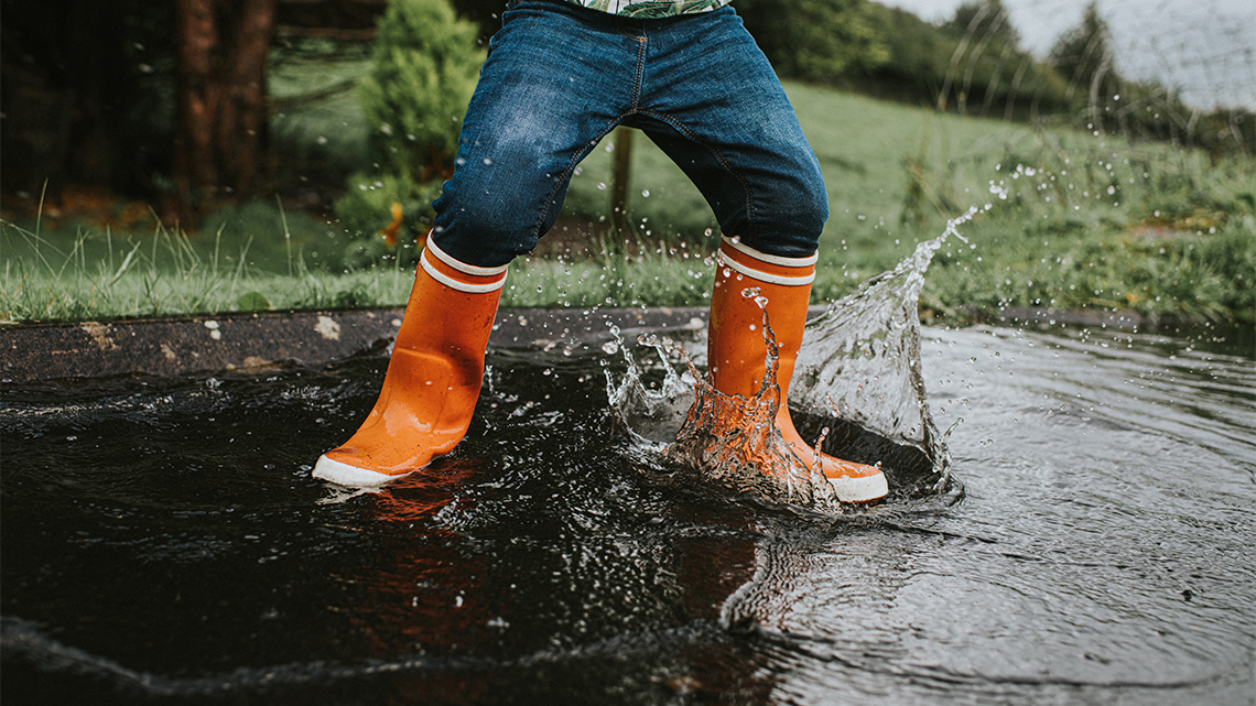 A child wearing rubber boots and splashing in a puddle.