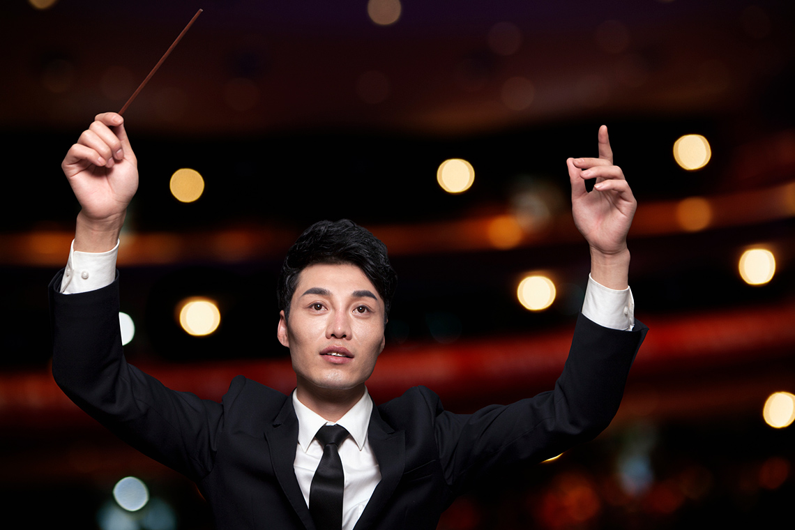A conductor with their arms raised holding a baton.