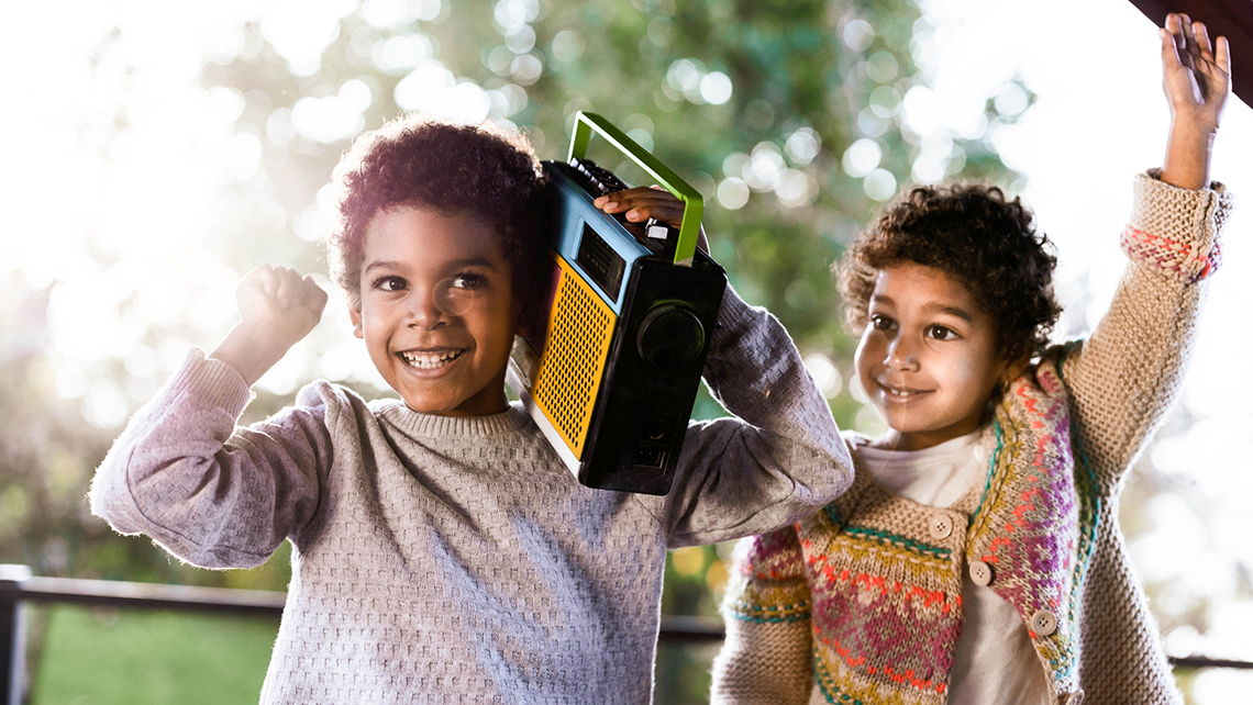 Two children listening to a portable radio outdoors.