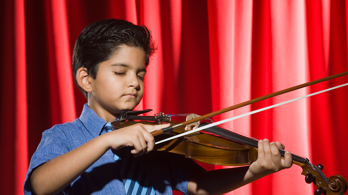 A child performing with a violin on stage.