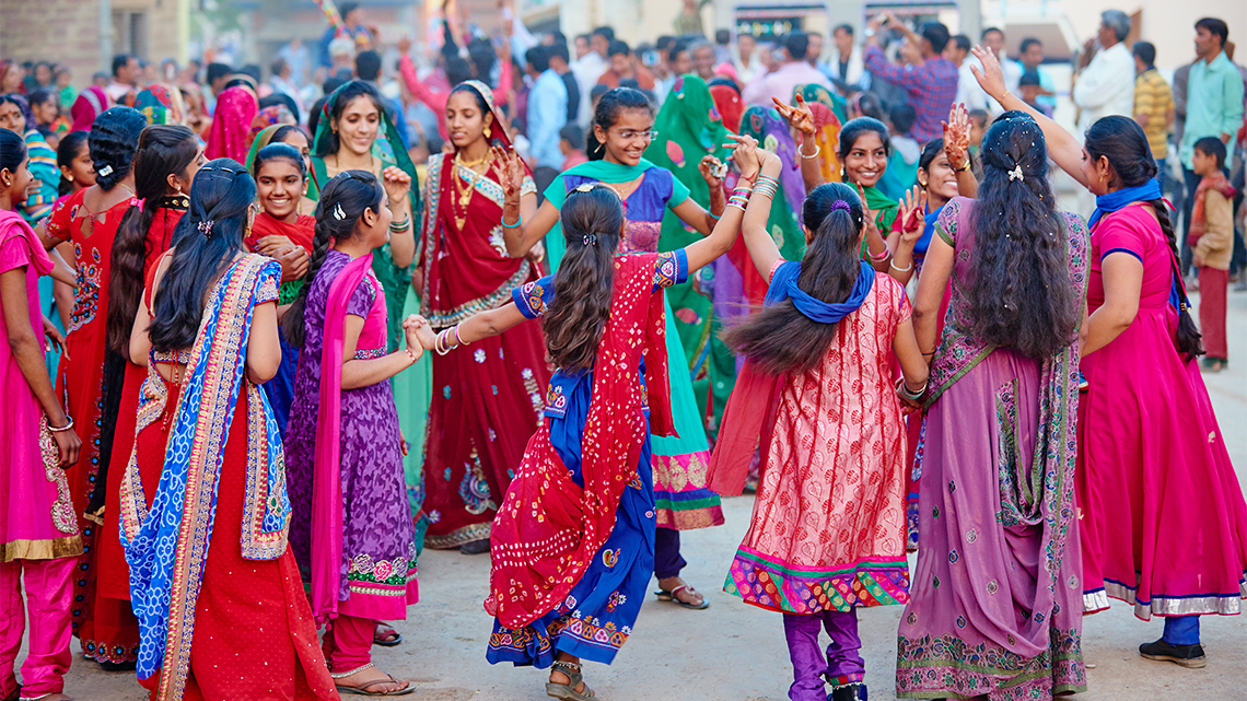 A group of people wearing colourful outfits and dancing to music in the street.