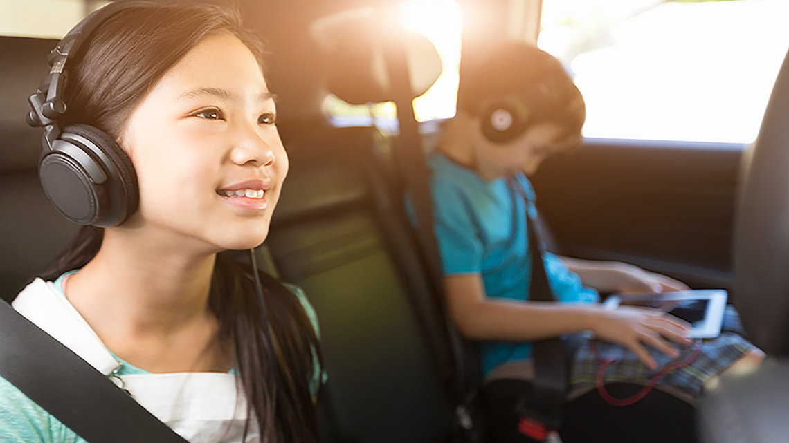 Two children wearing headphones and listening to music in the backseat of a car.