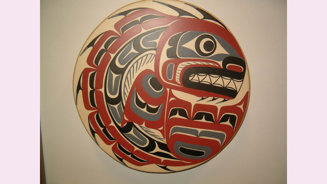 A round drum decorated with an Indigenous design of a fish.