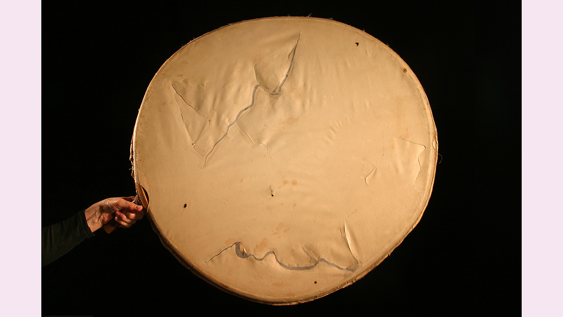 A large round drum with a wooden frame and a handle. A skin is stretched over the frame.