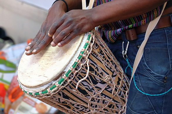 A person with their hands on a djembe drum. The drum is held between the legs when played.