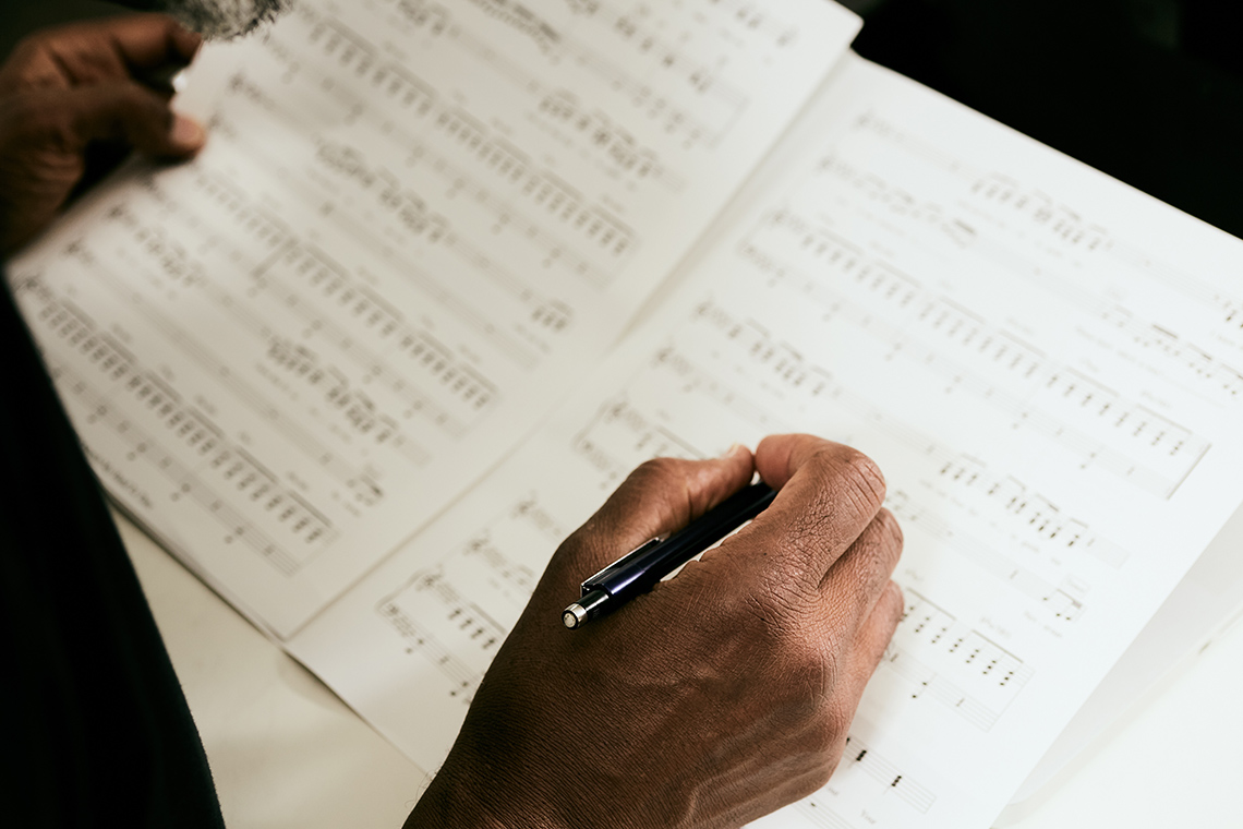 A hand holding a pen over sheets of music