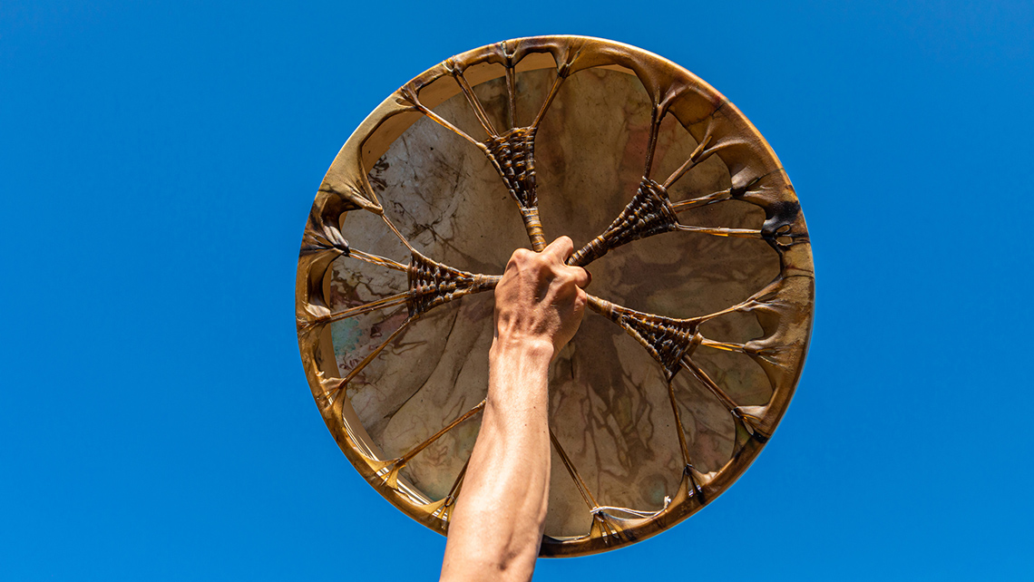 A person is holding up a flat, circular instrument with animal skin stretched the top.