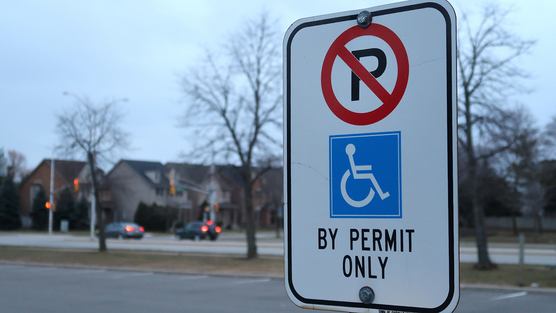 This sign has a P with a circle and red line through it. Under that is a blue accessible parking image and then the words, 'By Permit Only.'