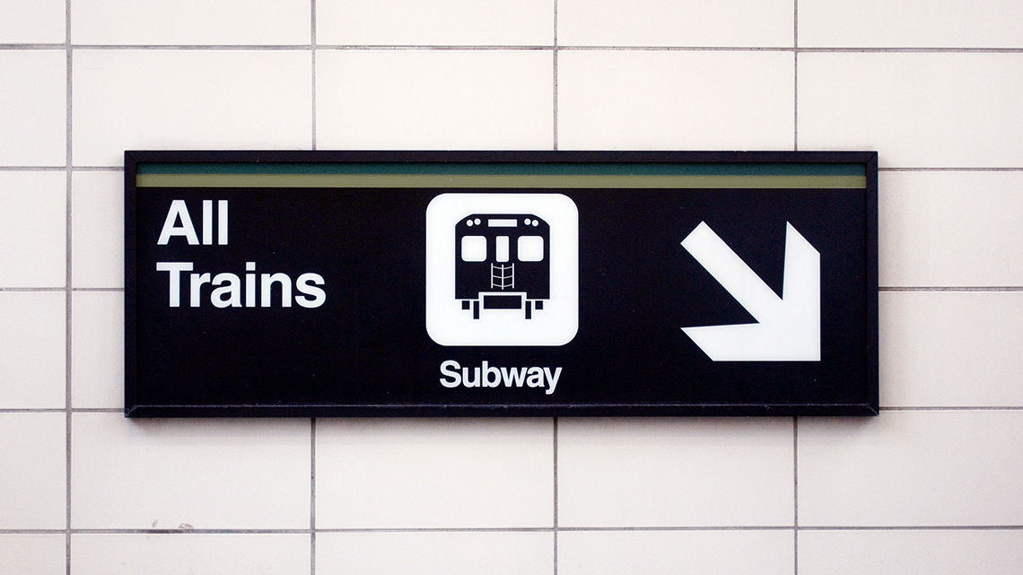 Subway sign that states All Trains and has an image of a subway car beside an arrow pointing down and to the right
