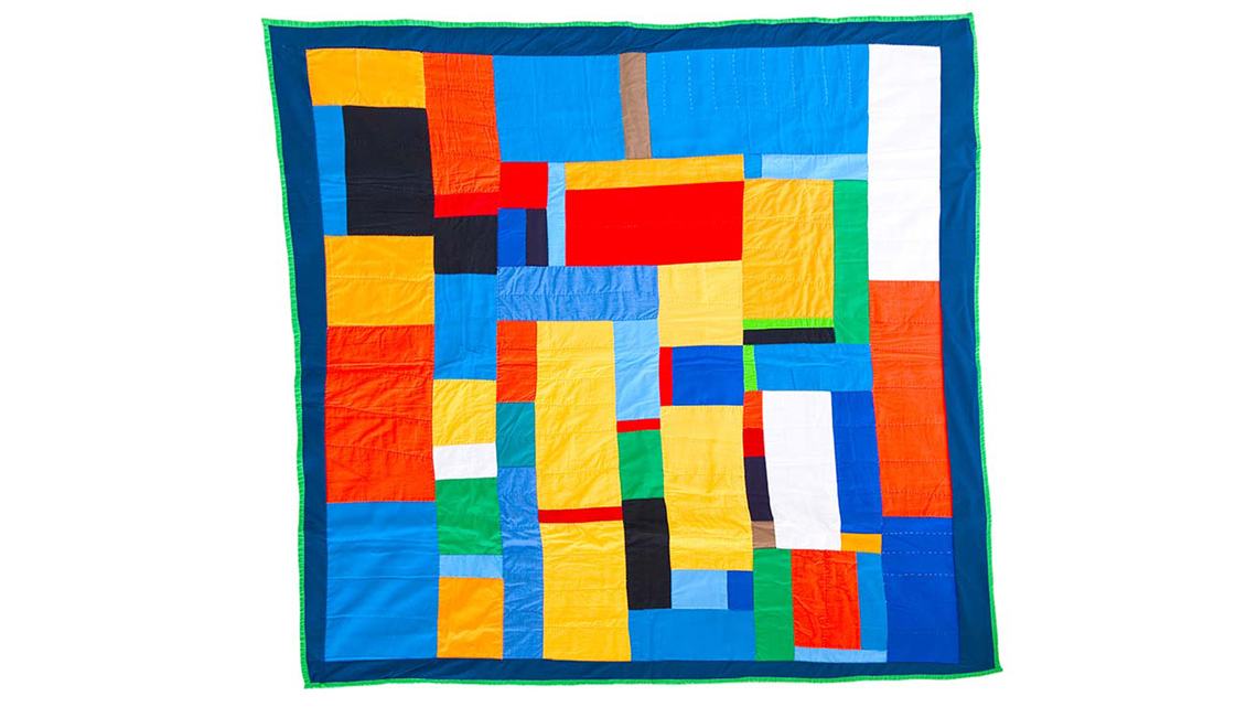 A geometric pattern of rectangles made from many vibrant pieces of quilted fabric.