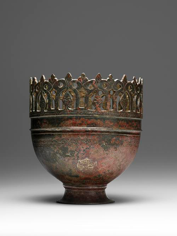 A bronze vase with a decorative edge cut out in an organic pattern.