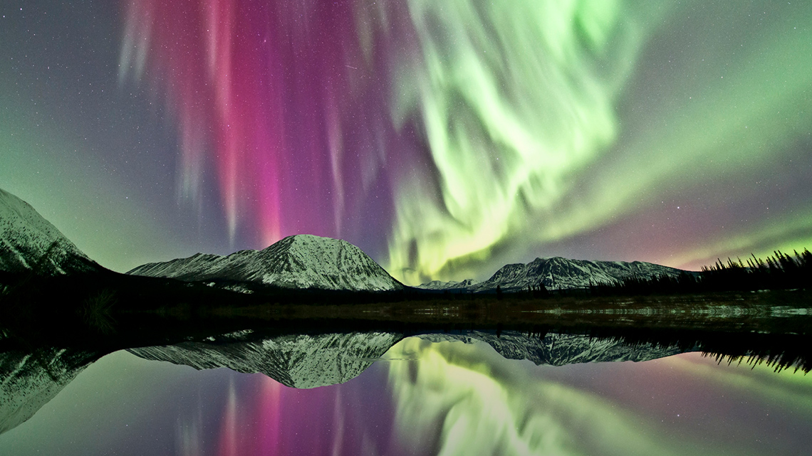  Northern lights above a lake and mountain landscape. 