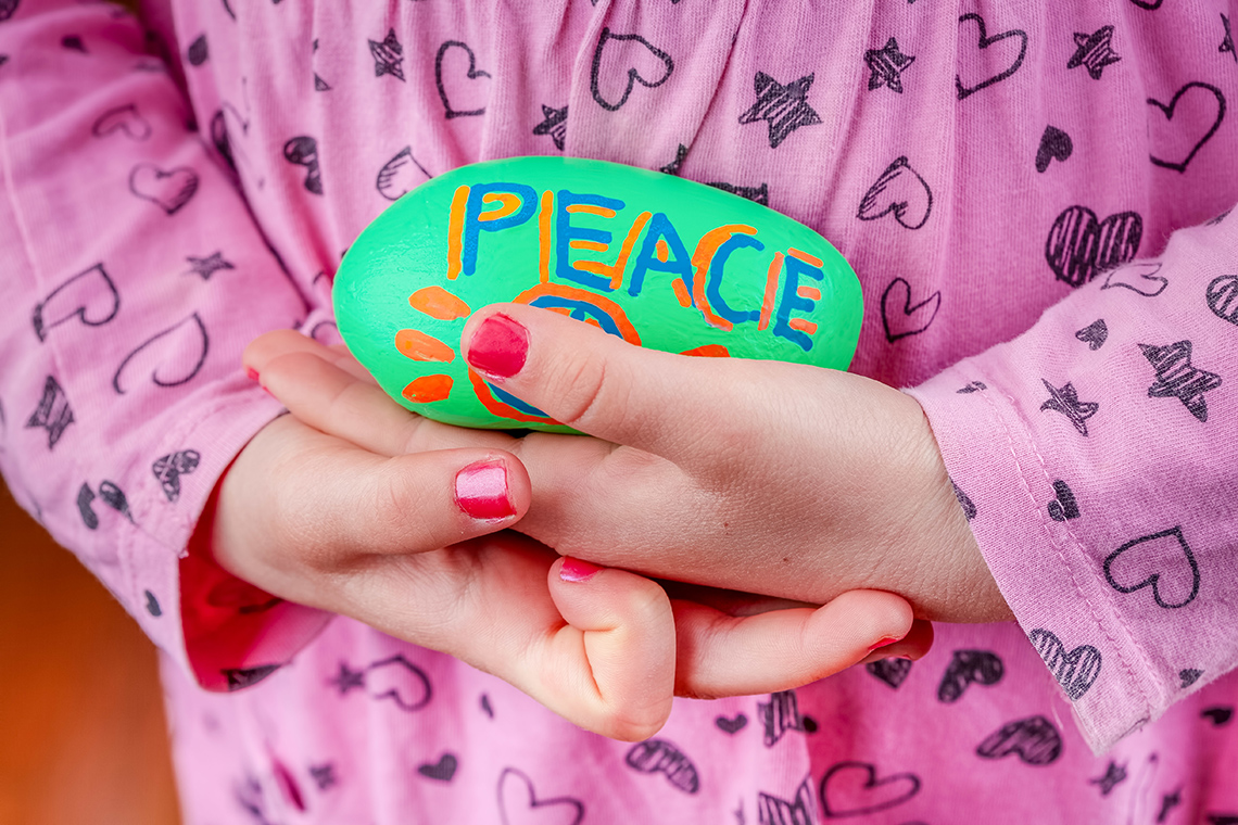 Kindness Rock A child holding a kindness rock with decorative dots and the word peace painted on it in bright colours