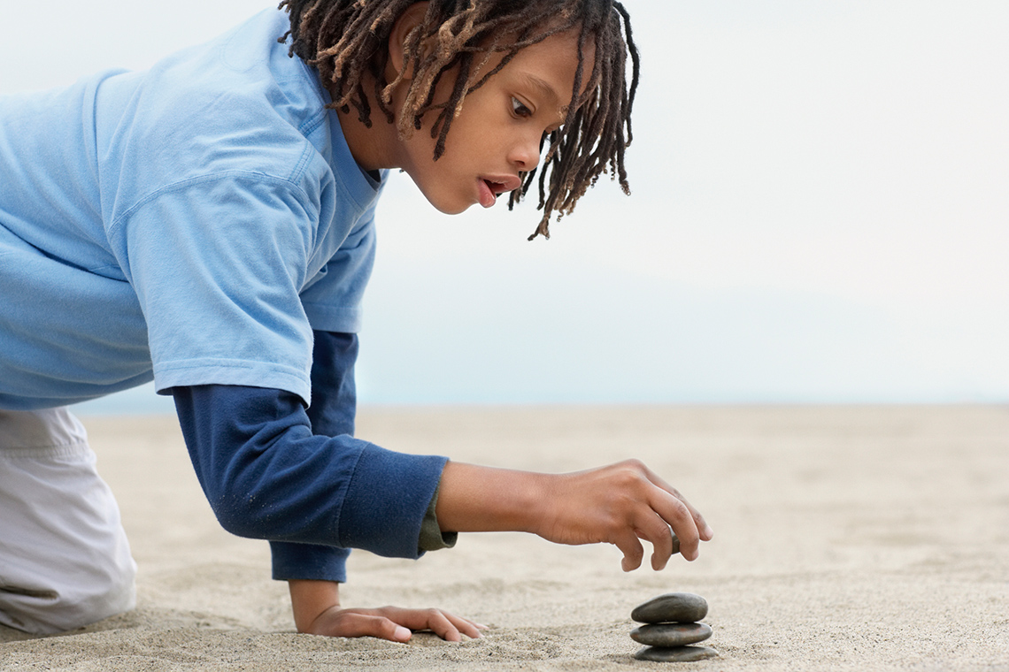 A student balancing small rocks on top of each other on a beach