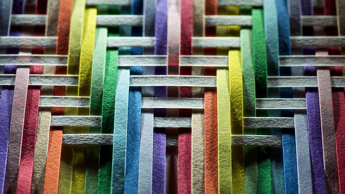 Close-up of a woven geometric pattern created from rainbow and white paper strips
