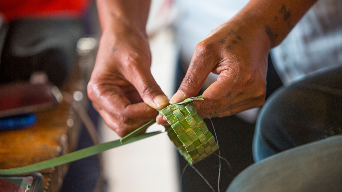 Two hands weaving bracelets from palm leaves