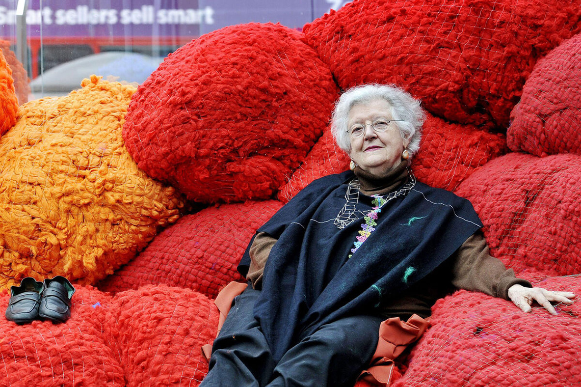 Sheila Hicks sits amongst large sphere sculptures made of yarn
