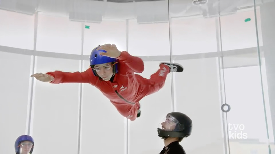 An athlete balancing horizontally with their arms and legs spread as they float in a vertical wind tunnel