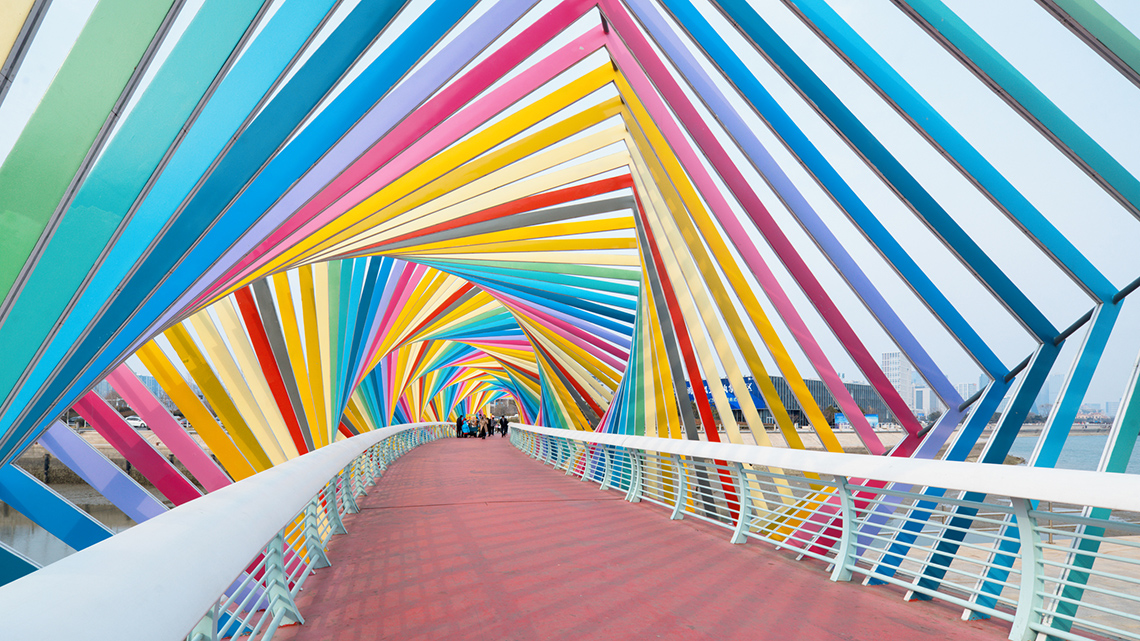 A bridge with a cover made of parallel, equally spaced diagonal lines that intersect and create a geometric rainbow pattern