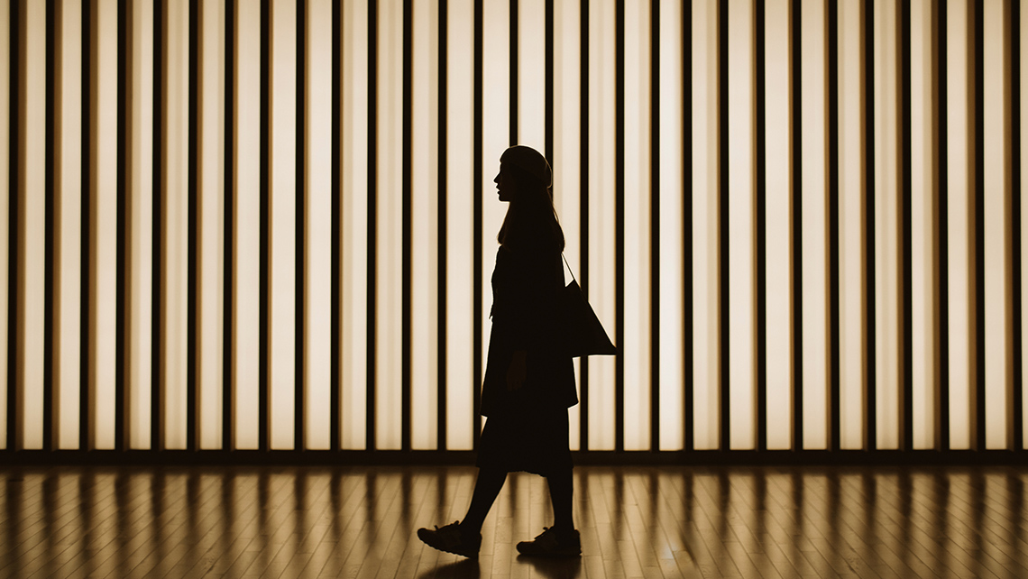 A person's silhouette in front of a lit backdrop made of a parallel, equally spaced vertical lines