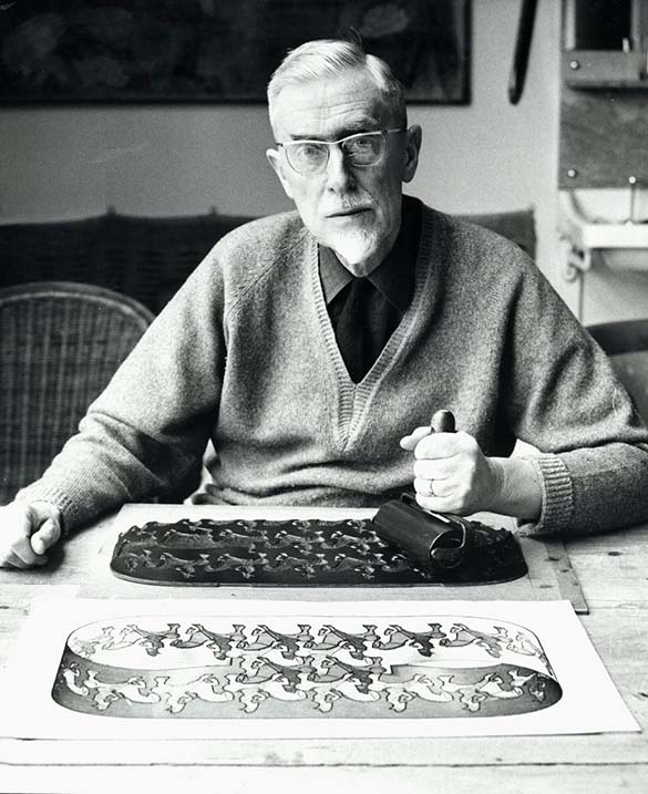 M.C. Escher in his studio making a print by applying ink to a woodblock with a brayer.