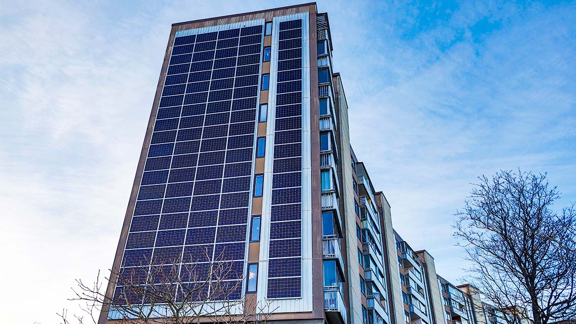 An apartment building with solar panels along the side of the building. The solar panels are placed in rows in between the balconies, from the top of the building to the bottom.
