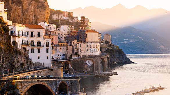 Many old buildings of diverse sizes built on the side of a cliff overlooking water.
