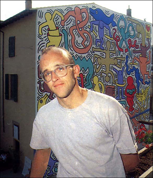 Keith Haring standing in front of his mural painted on the entire side of a three-storey building.