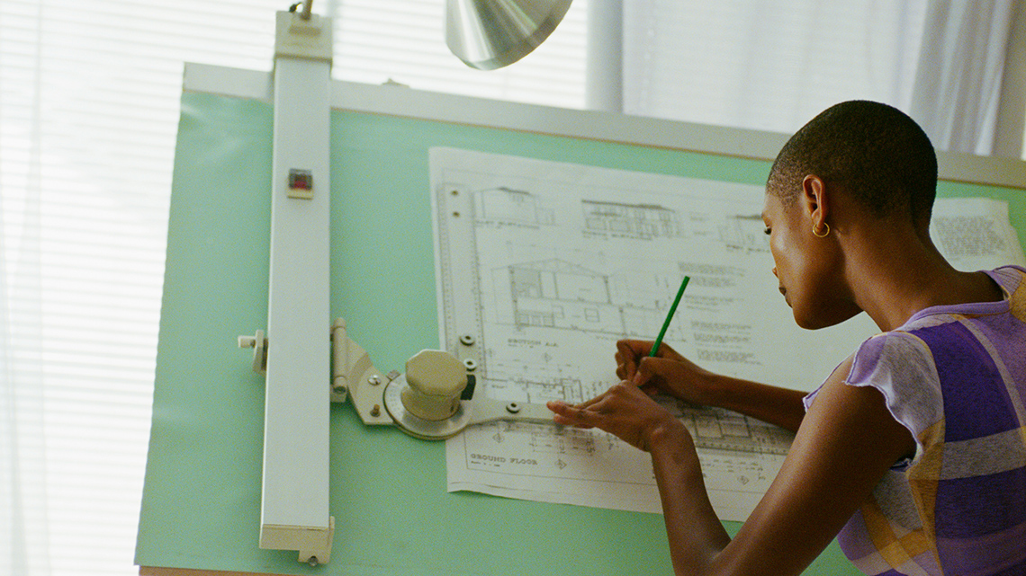 An architect drawing a building plan at a drafting table.