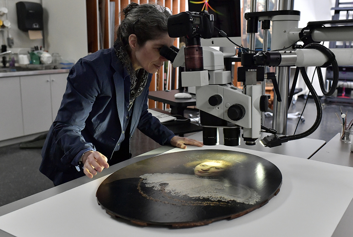 An art conservator uses a microscope to look at the fine details of a painting.