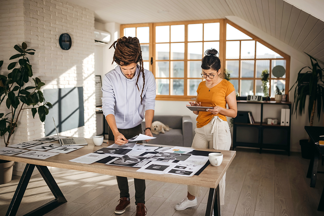 Two adults looking over different advertisement designs spread out on a table.