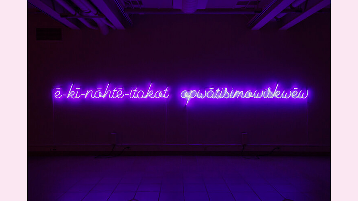 Purple neon letters in the Cree language with a dark purple background.