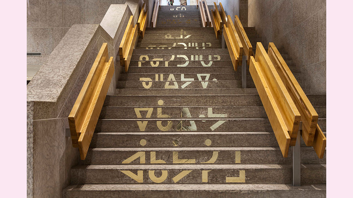 There is a cement flight of stairs photographed from below, with wooden handrails and letters in a foreign language written on the stairs.