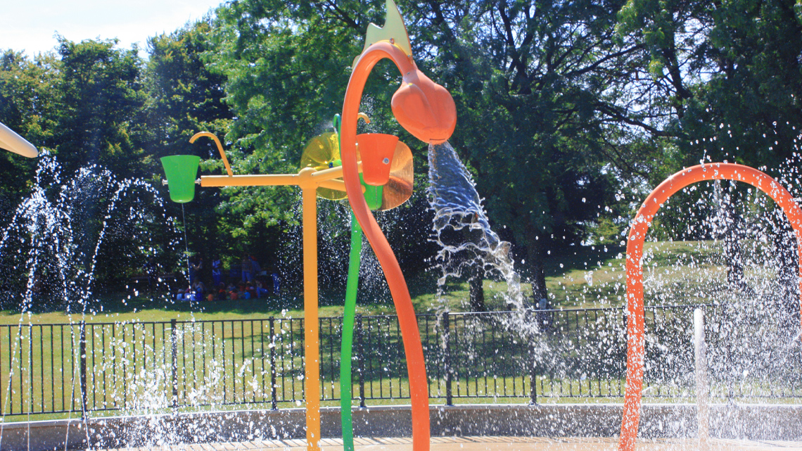 Different water play equipment in a playground. Some pour water from the top and some have water coming up from the ground.
