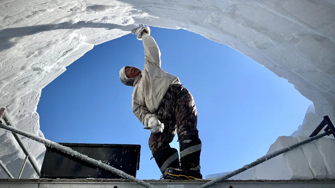 Soloman Awa building an igloo out of snow.