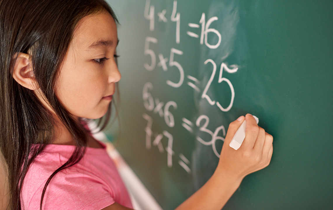 A student answering multiplication problems on a chalkboard.