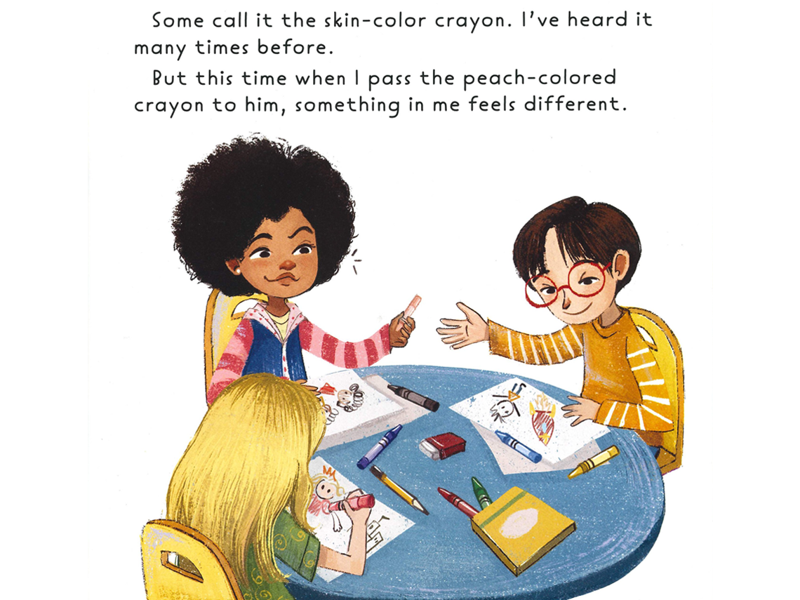 Three children sitting around a round blue table, drawing. The female student in the middle, with curly hair and medium brown skin hands the student next to her a peach-colored crayon.
